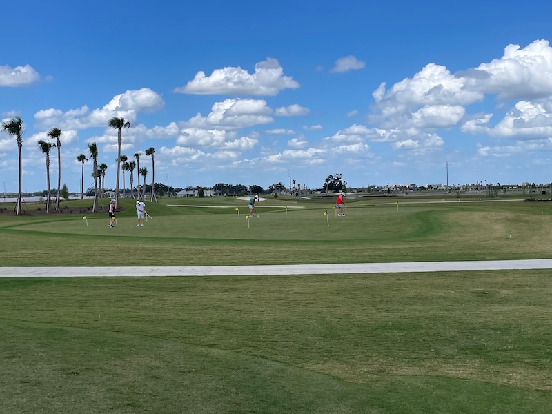 Practice green at Beautyberry with golfers putting under blue sky